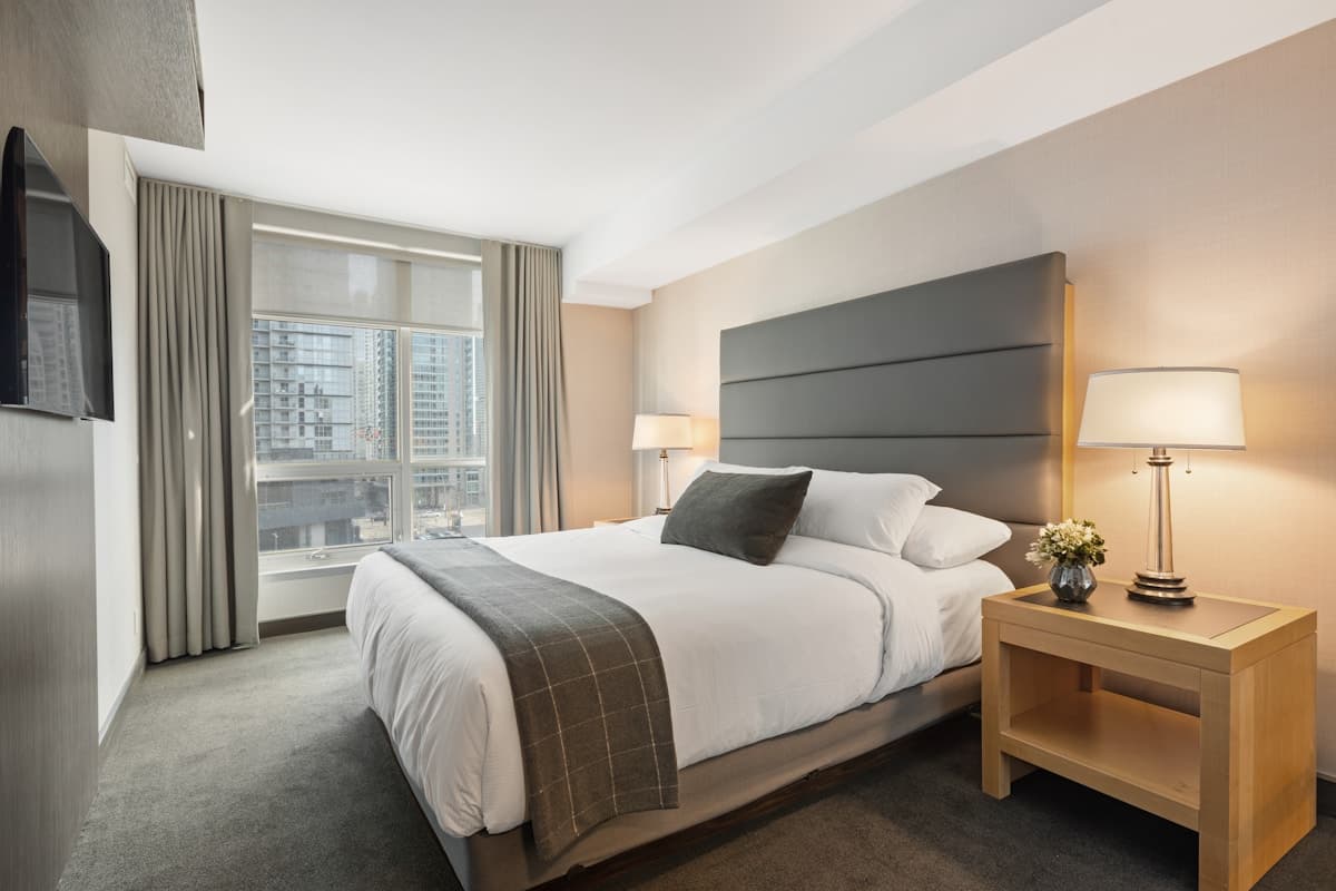 Finished hotel guest room with a wall-mounted television, bed, and nightstand lighting